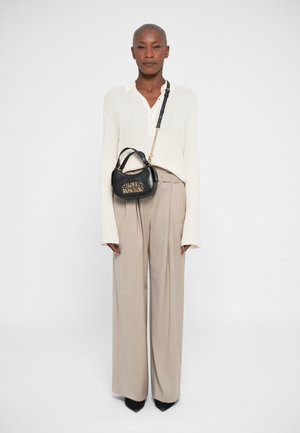 Black leather handbag with gold "LOVE MOSCHINO" lettering, sitting in a hand, paired with beige wide-leg trousers and a cream knit top.