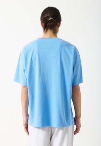 Svetlo modra bombažna majica s kratkimi rokavi, sproščenim krojem in okroglim izrezom. Ima gladko teksturo in preprost dizajn.