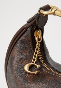 Gros plan d’un sac à main en cuir texturé marron foncé avec une fermeture éclair dorée et un tire-zip chaîne dorée en forme de lettre C.