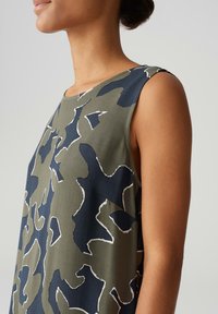Sleeveless top in olive green with abstract navy and white pattern, featuring a round neckline and a soft, smooth fabric texture.