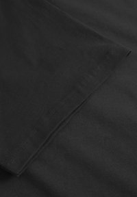 Close-up van zwarte katoenen T-shirtstof met een gladde textuur en een gevouwen mouwzoom met zichtbare stiksels.