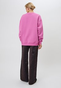 Felpa rosa oversize con maniche lunghe e scollatura a girocollo, abbinata a pantaloni neri larghi con motivo leopardato.
