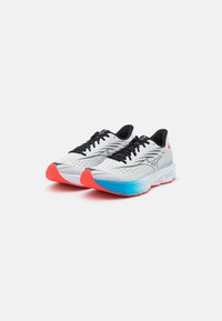 Scarpe da ginnastica bianche con superficie testurizzata, dettagli neri e suole colorate in blu e rosso. Presentano un design leggero e un sistema di allacciatura.