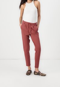 Roodbruine, relaxed-fit broek met een trekkoord in de taille, gecombineerd met een witte mouwloze top en laarzen met luipaardprint.