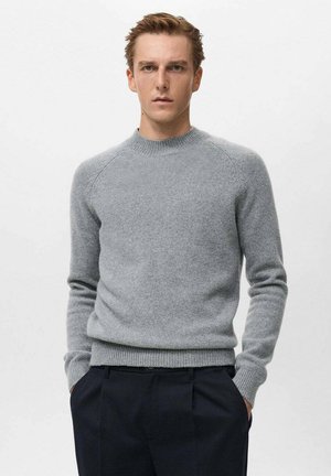 Suéter de punto gris con cuello redondo, puños acanalados y dobladillo acanalado. Presenta una textura suave y mangas tipo raglán. Combinado con pantalones oscuros.