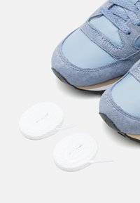 Lyse blå sneakers med en blanding av semsket skinn og syntetiske materialer, med hvite snørebånd og en svart gummisåle.