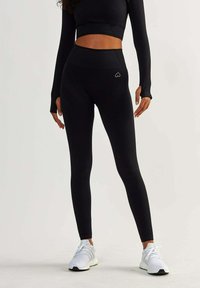 Black high-waisted leggings with a seamless design and textured pattern. Paired with a fitted long-sleeve top. White athletic shoes.