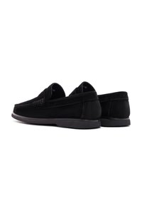 Mocasines de ante negro con una textura suave, punta redonda y suela de goma baja. Presentan detalles bordados en la parte superior y un diseño en general minimalista.