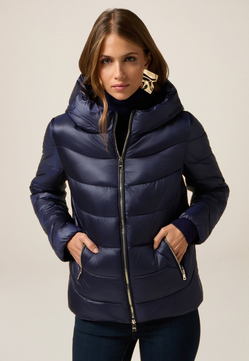 Marineblå pufferjakke med quiltet design, oversized hætte, lynlåslukning foran og sidelommer; lavet af glansfuldt, glat stof.
