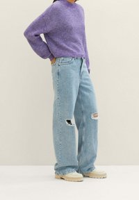 Pull violet en tricot avec un col rond, associé à un jean bleu clair ample avec des déchirures aux genoux et des chaussures beiges épaisses.
