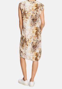 Hihaton mekko ruskeassa ja valkoisessa matelijakuosissa, valmistettu kevyestä materiaalista. Ominaisuuksiin kuuluu löysä istuvuus ja pyöristetty helma, yhdistettynä valkoisiin kenkiin.