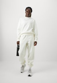 Hvid sweatshirt og matchende joggers i blødt stof med ribbede manchetter. Grå sneakers og en sort vandflaske fuldender outfittet.