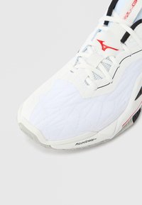 Λευκό αθλητικό παπούτσι με υφή στην επιφάνεια, ζιγκ-ζαγκ μοτίβο και κόκκινες λεπτομέρειες. Διαθέτει κορδόνια, στρογ γυλεμένη μύτη και ελαστική σόλα.