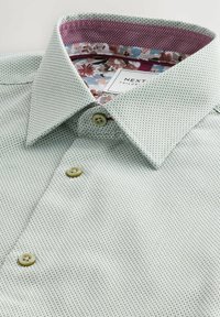 Hellgrünes, strukturiertes Hemd mit einem gemusterten Innenkragenfutter in maroon und floralem Design sowie zwei hellen Knöpfen.