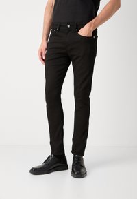 černé slim-fit džíny, bavlněný materiál, pět kapes, zip s knoflíkovým zapínáním, jemné švy, spárováno s černými koženými botami.