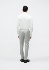 Calças cinza claro, ajustadas, com bolsos frontais e traseiros, combinadas com uma blusa branca de mangas longas. Sapatos pretos, de textura suave, com design minimalista.