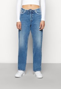 Ljust blå, avslappnat sittande jeans med dragsko i midjan, fickor fram och bak, samt en urtvättad textur. Matchas med vita sneakers.