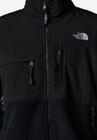 Czarna kurtka z teksturowanym polarem i gładkim, górnym materiałem. Posiada kieszenie na zamek, wysoki kołnierz oraz logo The North Face na piersi.
