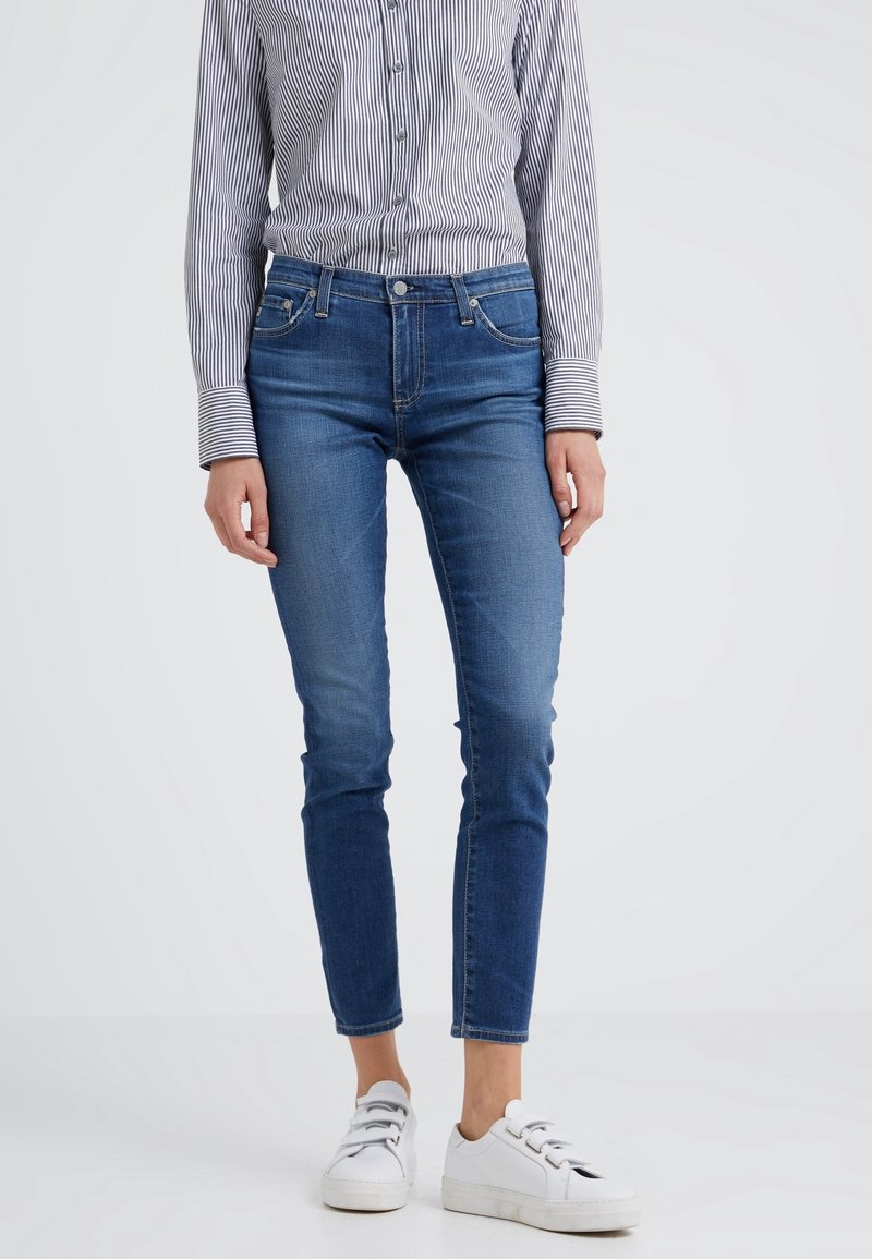 Tighta blå jeans i denim med medelhög midja, fem fickor och lätt blekning. Kombinerat med en randig långärmad skjorta och vita sneakers.