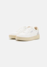 Des baskets blanches avec une tige en cuir lisse, une semelle en caoutchouc beige et de subtils accents gris à l'arrière. Design à laçage.