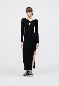 Rochie neagră tricotată cu dungi, mâneci lungi, decolteu rotund cu un detaliu decupat și fente laterale. Asortată cu teniși negri.