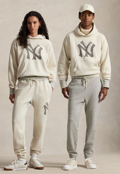 Pasujące zestawy casualowe zawierające jasnobeżowe i szare bluzy z kapturem z nadrukiem logo, kieszeniami typu kangur oraz tapered joggers z miękkiego materiału.