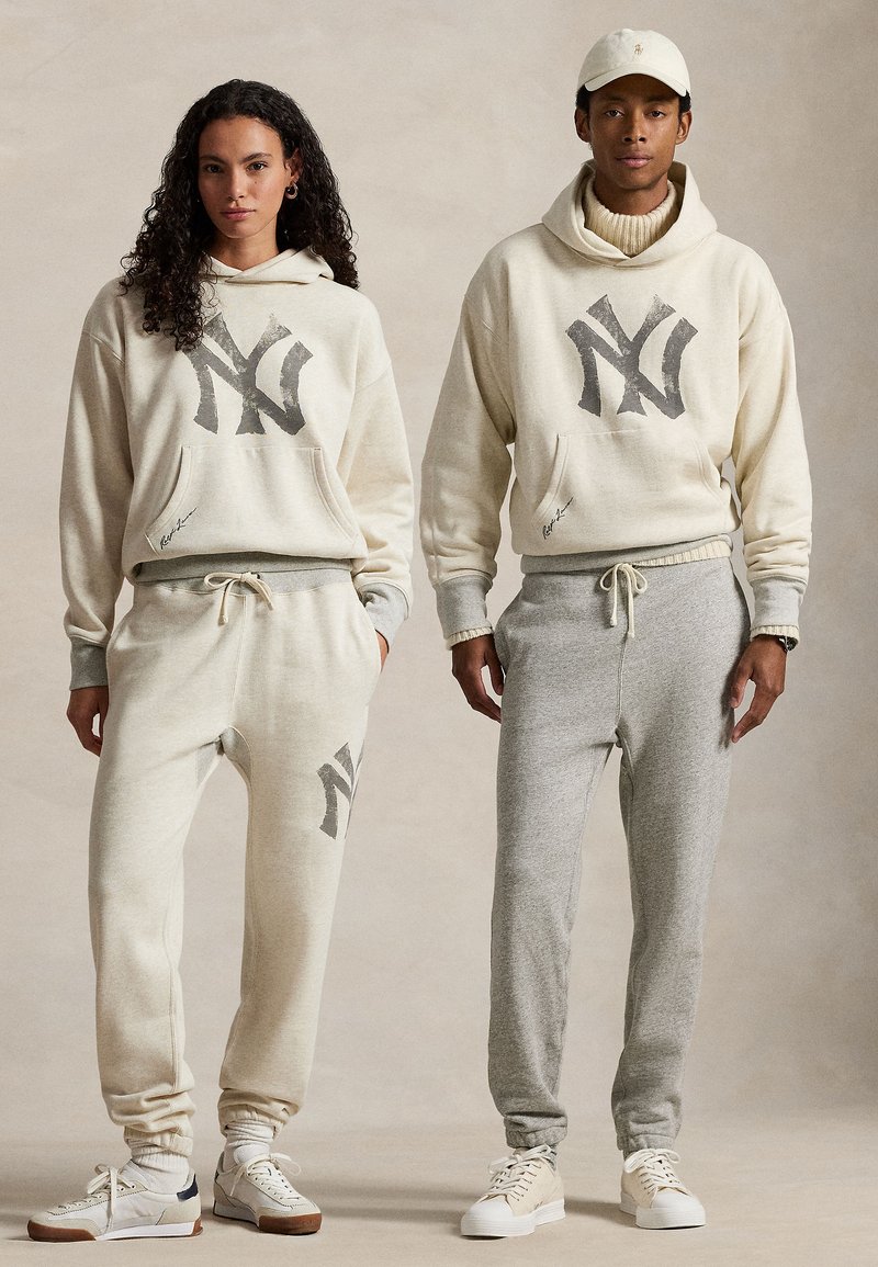 Σετ casual που ταιριάζουν, περιλαμβάνοντας ανοιχτό μπεζ και γκρί φούτερ με λογότυπα, τσέπες pouch και tapered joggers από μαλακό ύφασμα.