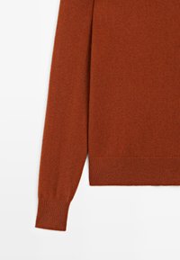 Rostfarbener gestrickter Pulloverärmel und -saum mit gerippten Bündchen und unterem Saum auf einem weißen Hintergrund.