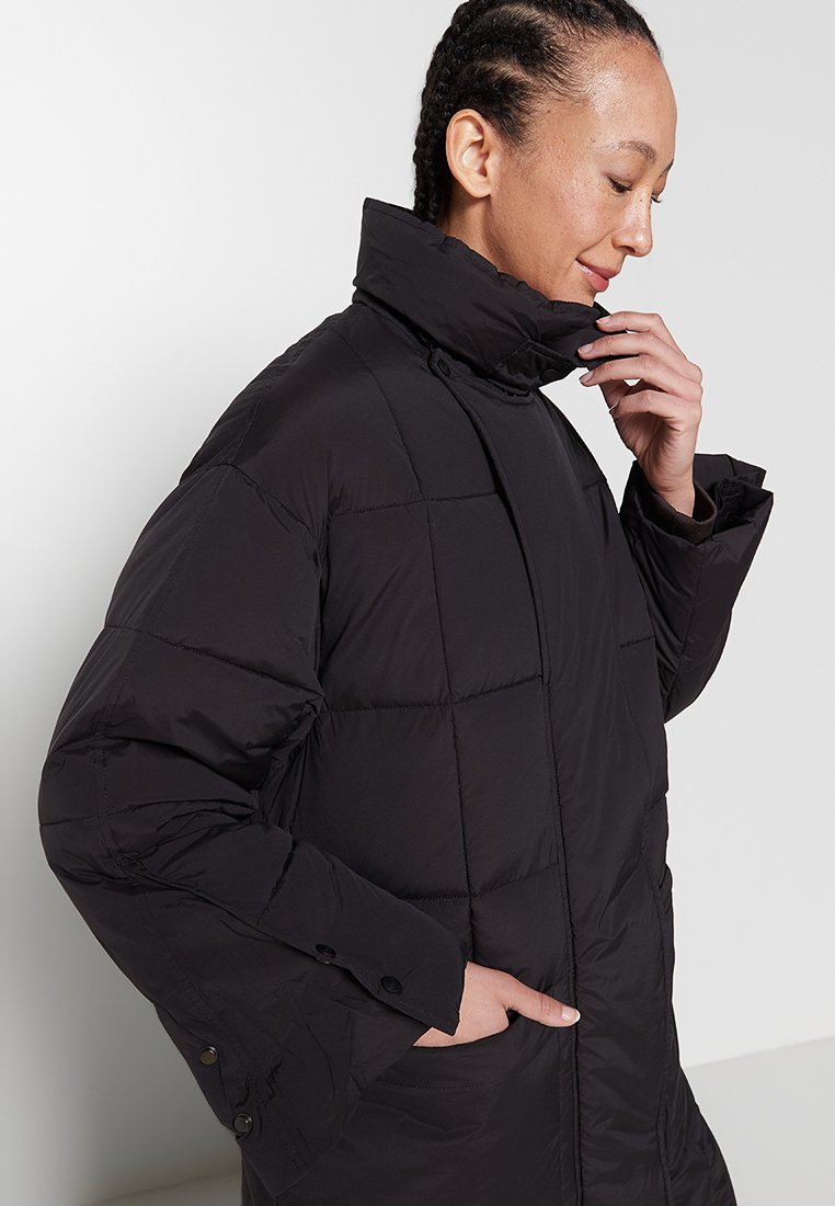 Schwarze Steppjacke mit gestepptem Design, hohem Kragen und geknöpften Ärmeln. Sie verfügt über einen glatten, strukturierten Stoff und seitliche Taschen.