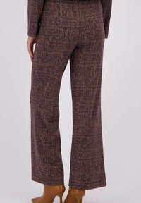 Uitlopende broeken in een gestructureerde bruin-oranje stof, met een geweven patroon. Gecombineerd met lichtbruine, puntige hakken.