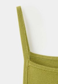 Gros plan d'un haut tricoté vert olive avec bretelle étroite et coutures visibles sur fond clair.