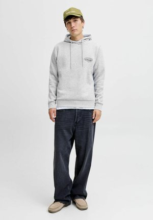Grauer Hoodie mit Logo auf der Vorderseite, Kordelzügen und gerippten Bündchen, kombiniert mit dunklen Jeans und einer hellgrünen Kappe. Weicher Stoffeinsatz.