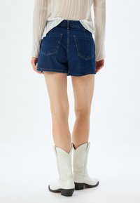 Shorts en denim bleu foncé avec une coupe décontractée et deux poches arrière. Associés à des bottes de cowboy blanches avec des coutures décoratives.