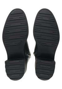 Botas de tobillo de cuero negro con una suela de goma texturizada que presenta surcos horizontales y un tacón cuadrado. Branding visible en la suela.