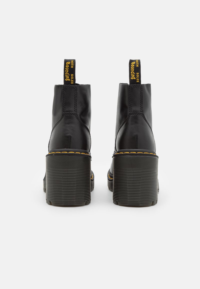 Schwarze Leder-Ankle-Boots mit einer klobigen gerippten Sohle und gelben Akzentnähten, ausgestattet mit einer Zuglasche für einfaches An- und Ausziehen.