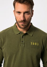 Mörkgrön polo skjorta i mjuk tyg, med krage, tre knappar i placket och broderad "1880 Legendary" detalj i kontrasterande färg.
