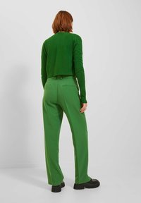 Groene gebreide cropped trui en groene hoge taillebroek met zijzakken en een gladde textuur. Zwarte platform schoenen maken de outfit compleet.