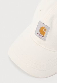 Εκρού υφασμάτινο καπέλο Carhartt με κυρτή γείσο και ραμμένη τετράγωνη ετικέτα με πορτοκαλί έμβλημα και όνομα της μάρκας.