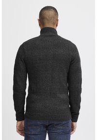 Mørkegrå strikkegenser med høy krage, strukturert mønster og ribbestrikkede ermer og nederkant. Brukt med blå jeans, og viser en avslappet passform.
