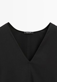 Černý oděv s hlubokým výstřihem do V, vyrobený z hladkého materiálu a minimalistického designu. Na límci je štítek s nápisem "Massimo Dutti".