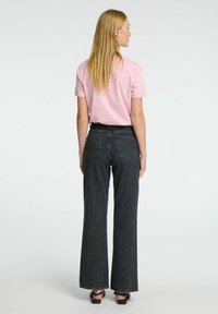 Camiseta rosa de manga corta combinada con pantalones vaqueros negros de pierna ancha. Los pantalones tienen una cintura alta y bolsillos traseros, con un ligero deshilachado en el dobladillo.