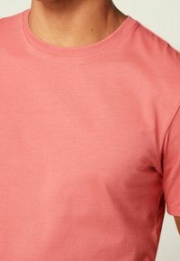 Jasnoróżowa koszulka z krótkim rękawem, okrągłym dekoltem i gładkiego materiału bawełnianego, o luźnym kroju i minimalnych detalach przeszycia.