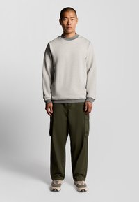 Grijze sweatshirt met een geribbelde halslijn, gecombineerd met olijfgroene cargobroeken. De outfit heeft zakken en beige sneakers met een grijs accent.