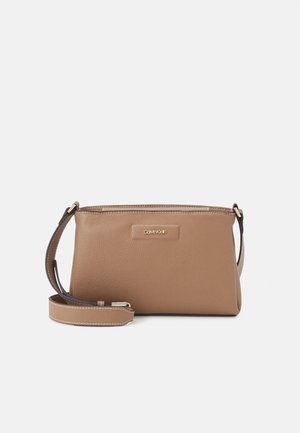 Brązowa skórzana torebka Calvin Klein na ramię z regulowanym paskiem i złotą plakietką z logo z przodu na białym tle.