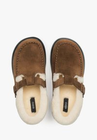 Brązowe zamszowe klapki z futrzanym wykończeniem, regulowanym paskiem i czarną gumową podeszwą. Okrągły czubek i przeszycia na krawędziach.