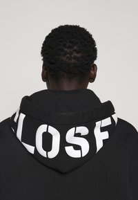 Zwarte hoodie met witte grafische tekst op de capuchon. Fleece materiaal met een zachte textuur en een relaxte pasvorm.