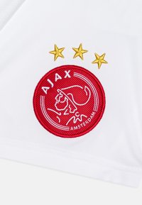 Tessuto bianco con logo Ajax ricamato in rosso, caratterizzato da una testa di leone e il testo "AJAX", arricchito da tre stelle d'oro sopra il logo.