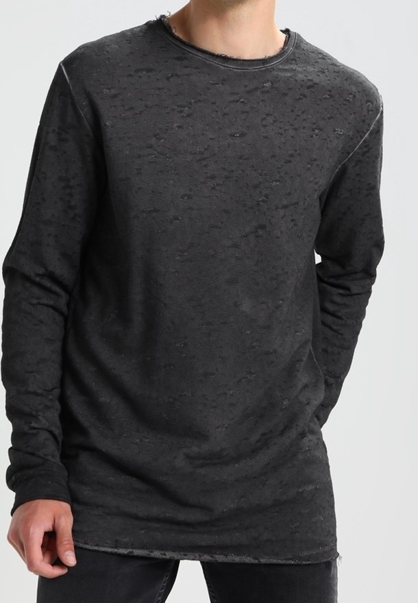 Homme portant un t-shirt noir à manches longues avec texture, col rond effiloché et coupe décontractée, debout devant un fond uni.