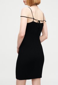 Μαύρο φόρεμα από ριμπ πλεκτό ύφασμα με λεπτές λεπτές τιράντες και δεσίματα στο πίσω μέρος. Τελειώνει πάνω από το γόνατο με κυμματιστό τελείωμα.