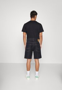 Mörkblå denimshorts med klassisk skärning, med bakfickor och en läderlapp vid midjan. Bärs med en svart t-shirt och vita strumpor.